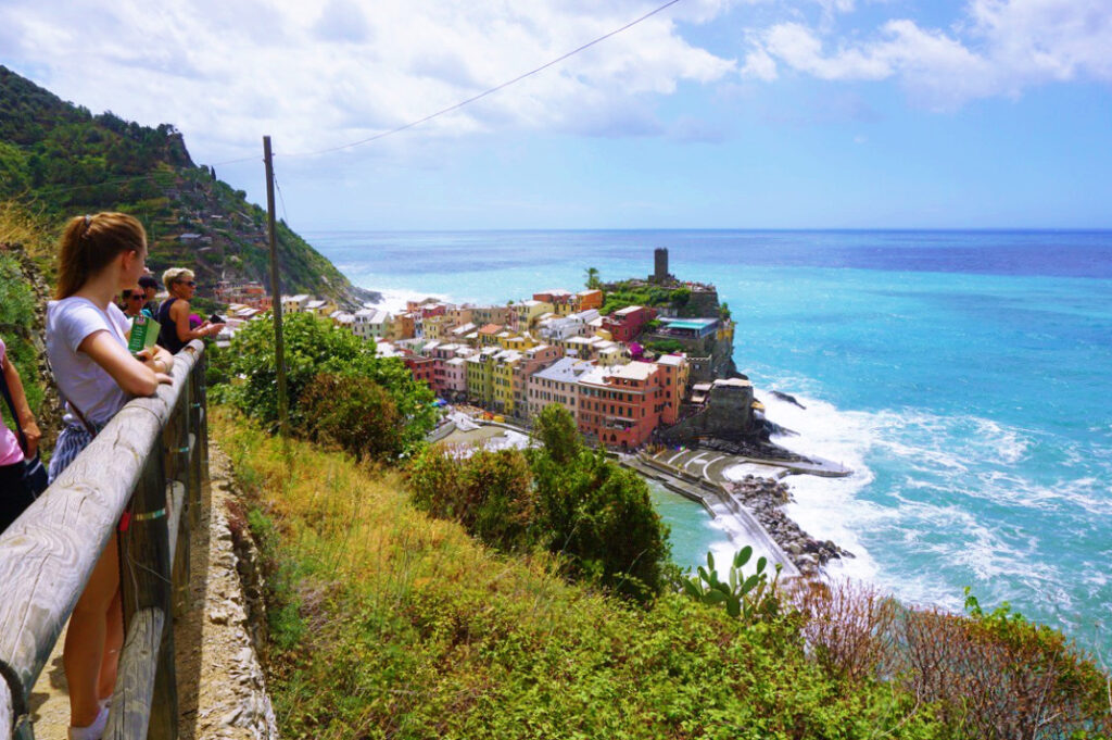 light and dark blue ocean against colorful town in cinque terre with a tourist looking out at the view