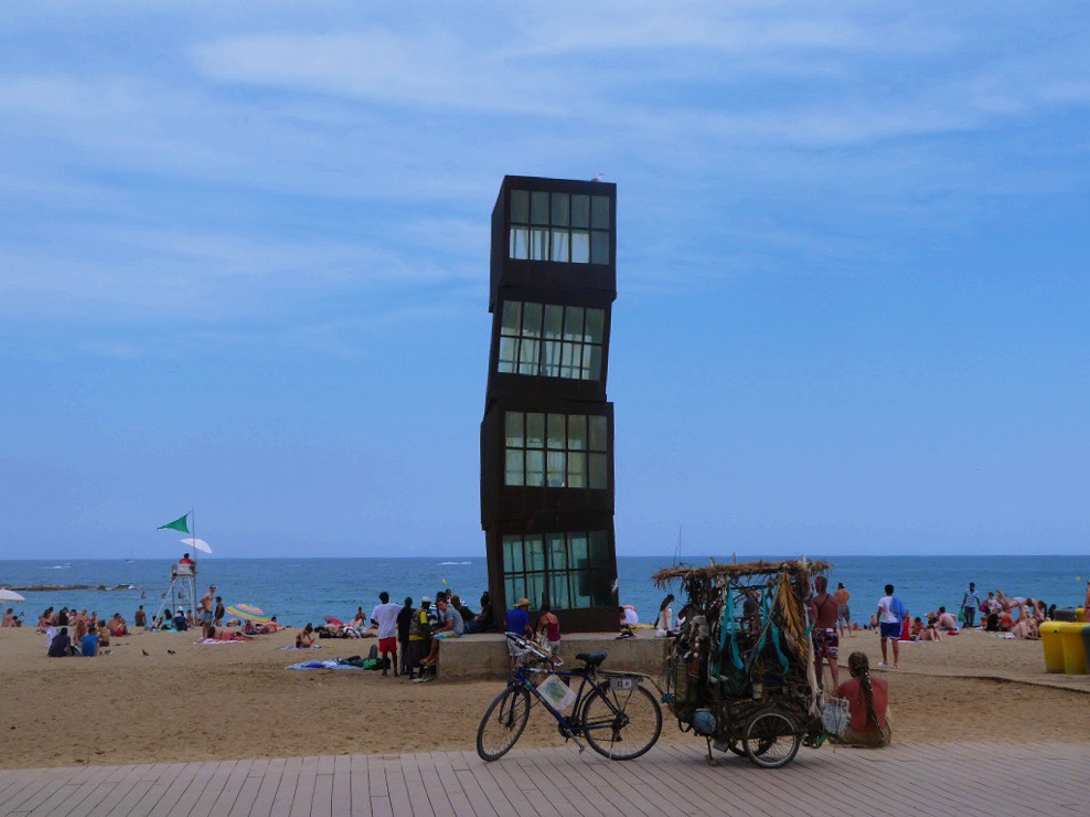 tall tower art structure on the beach of barcelona with blue sky