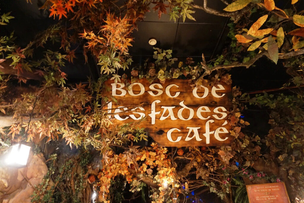 wooden sign for the bosc de les fades cafe surrounded by fake leaves