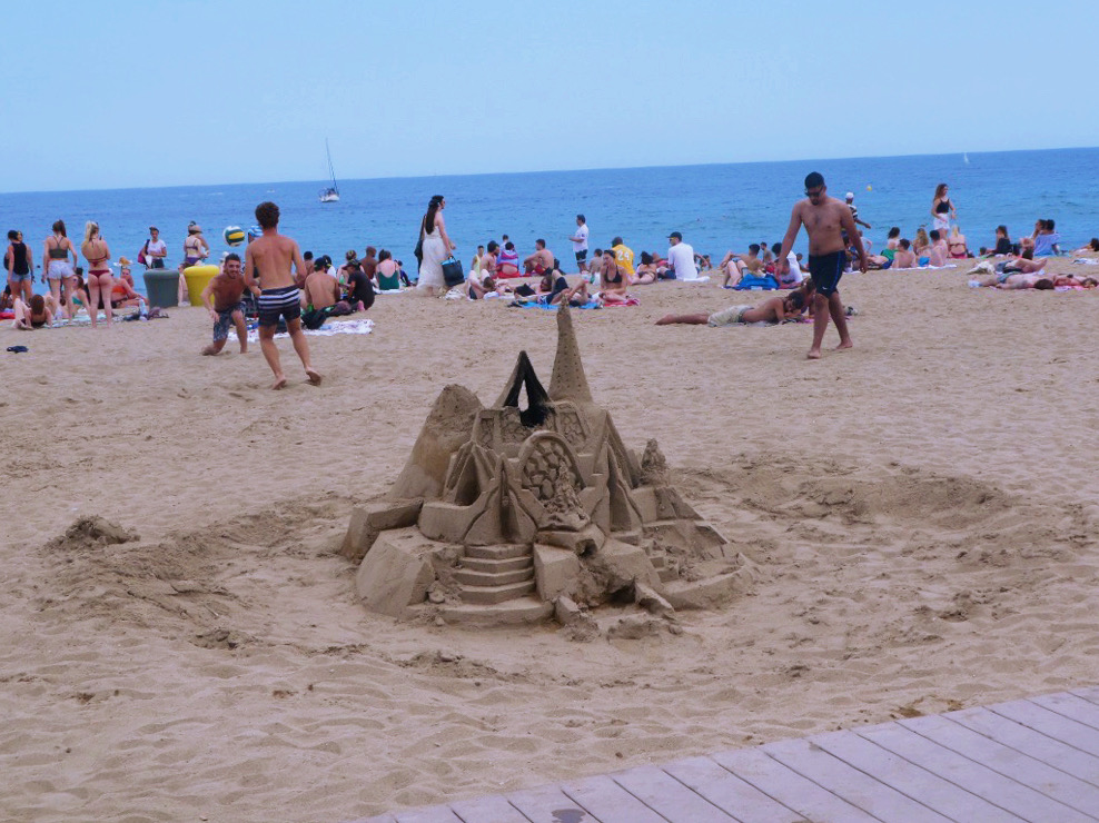 giant sand castle with people in the background on barcelona beach