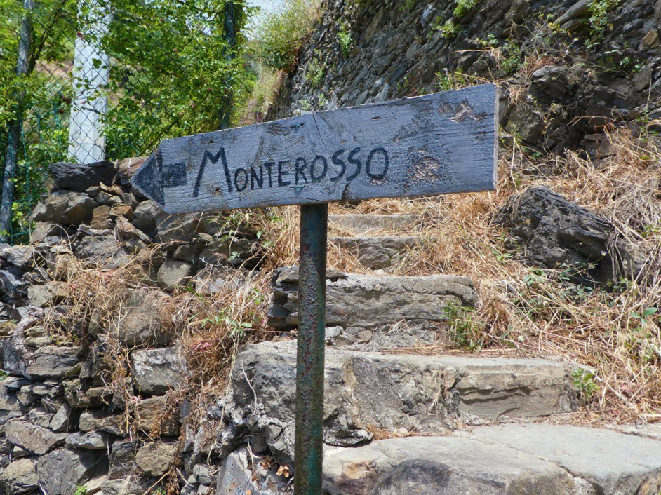 wooden sign to monterosso in front of stone steps on the dirt trail