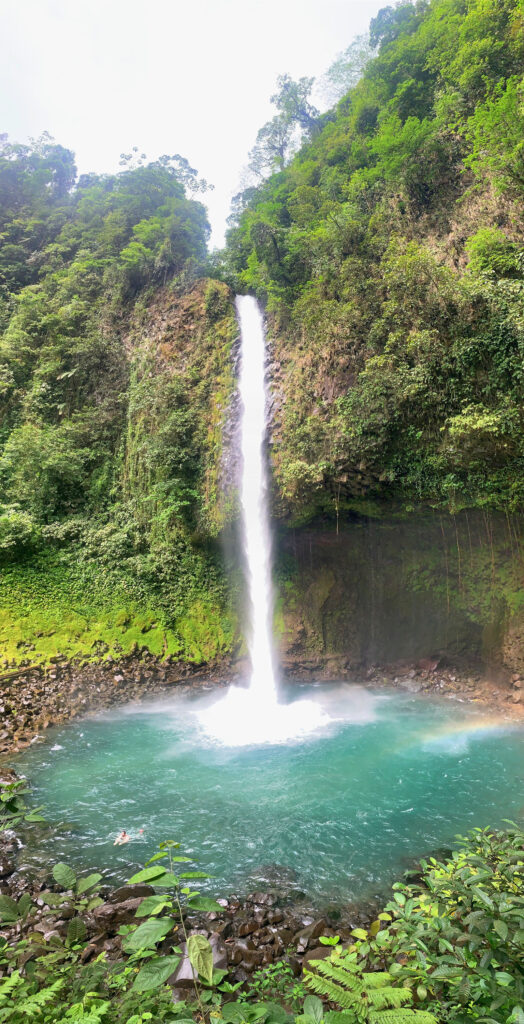 tall white waterfall feeding into small bright blue natural river with green trees