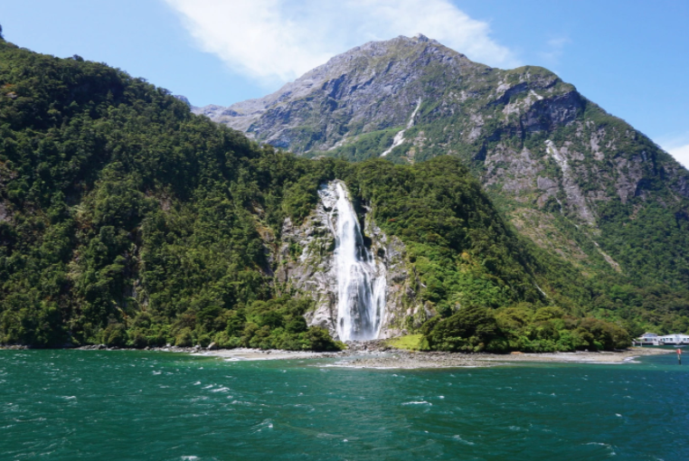 lady bowen falls in milford sound, white running water, tree covered mountains, blue tasman sea