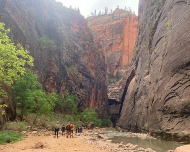 people walking below large red rocks by river