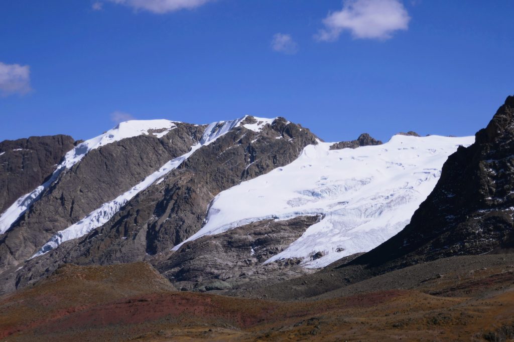 a close up of the receding snowy glaciers between dark rock and blue sky on the hike to rainbow mountain