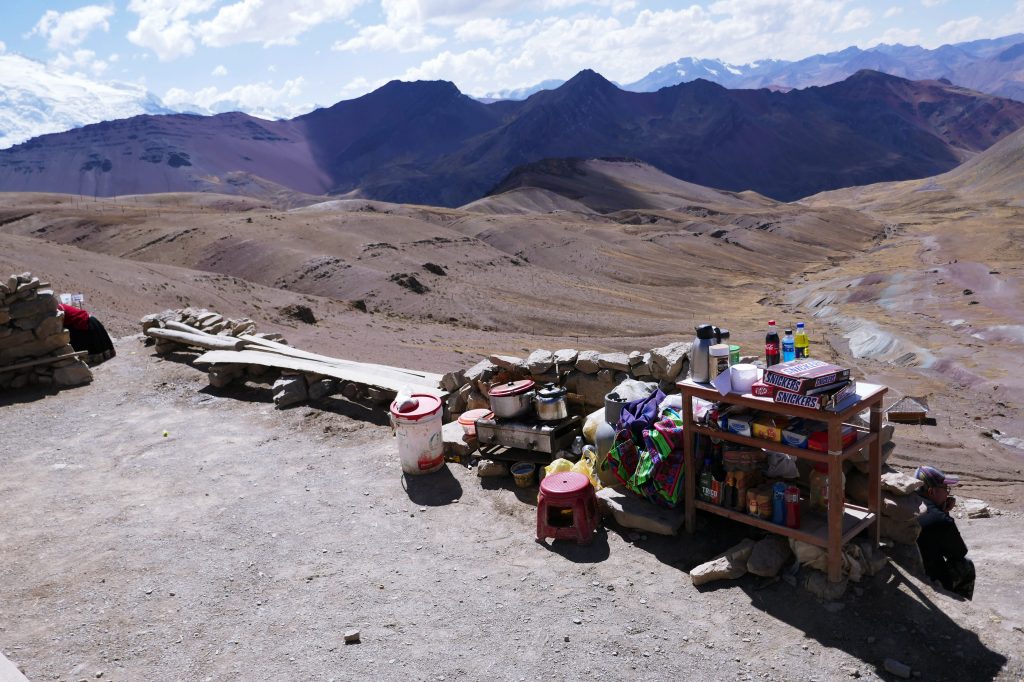 pile of snacks, pots, drinks, and souvenirs at the top of rainbow mountain with the andes in the background