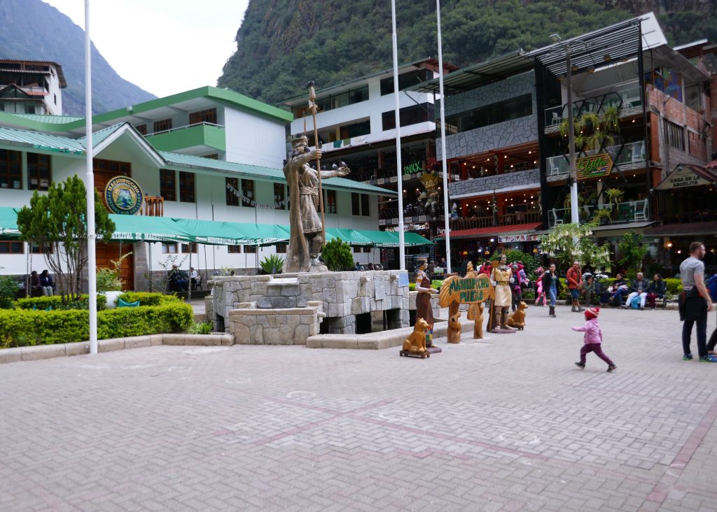 statue in the middle of an open plaza with storied building behind it