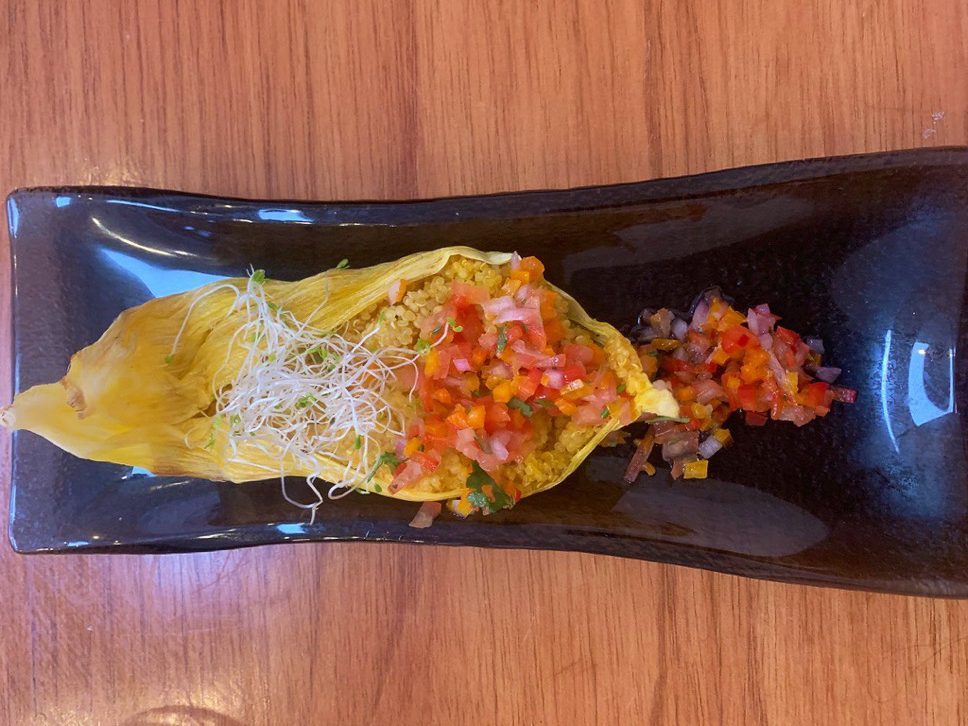 traditional cusco tamale with quinoa, bright tomatoes, and garnish on a dark blue rectangular plate on a wooden table