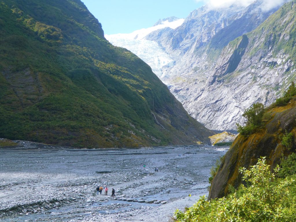 hikers walking through the stone river basin leading up to franz josef glacier
