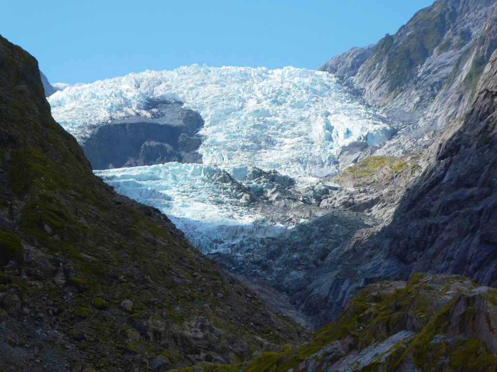 icy glacier surrounded by rock mountains with blue sky in the background