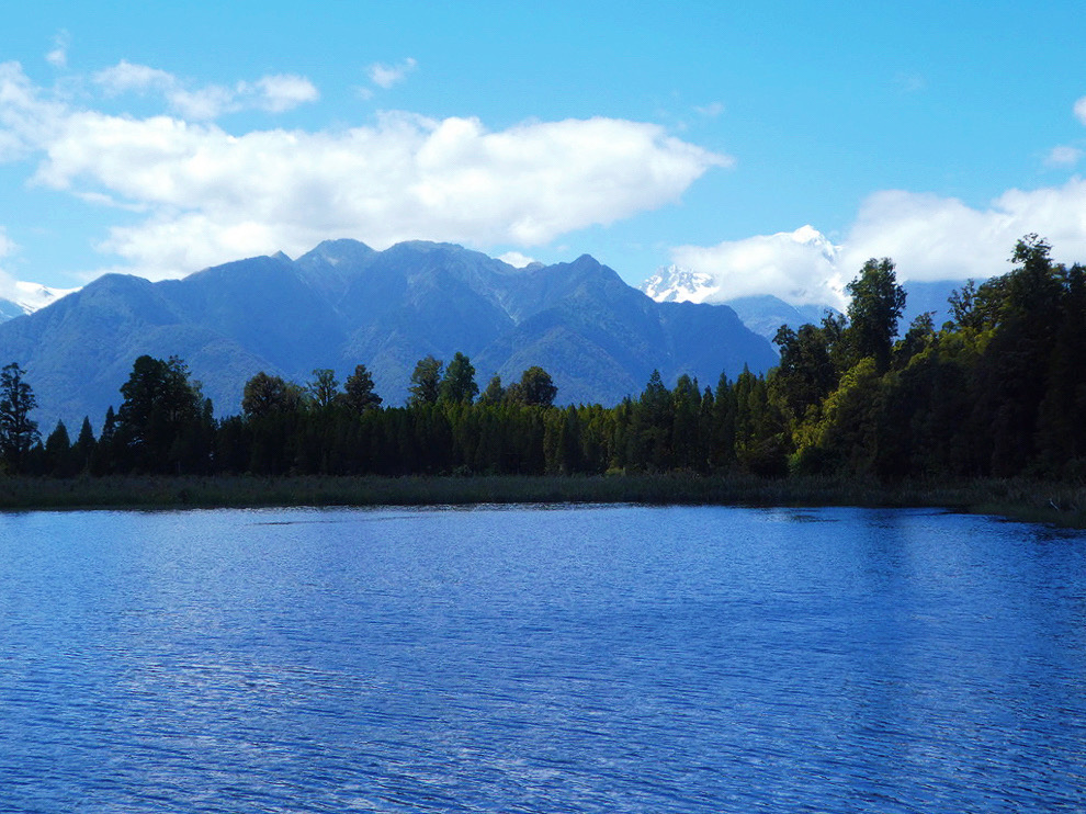 deep blue water with dark green trees and mountains