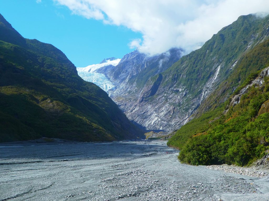 stone valley leading up to franz josef glacier with green trees
