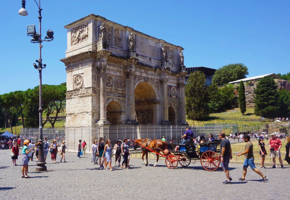 a horse carriage and people walking in front of the large arch of constantine