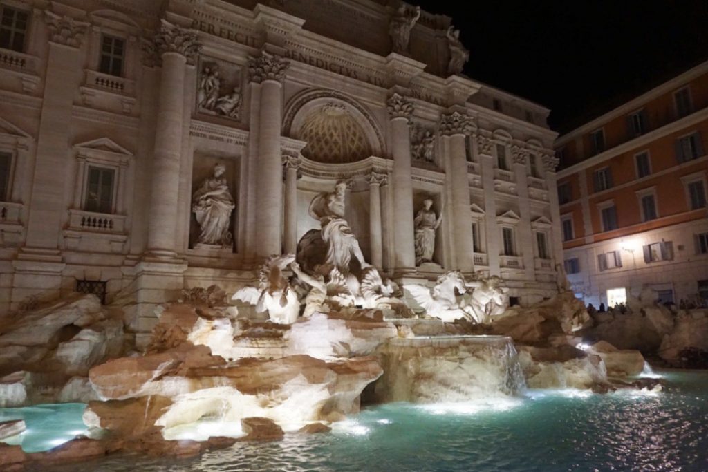 lights shining on statues in front of blue fountain