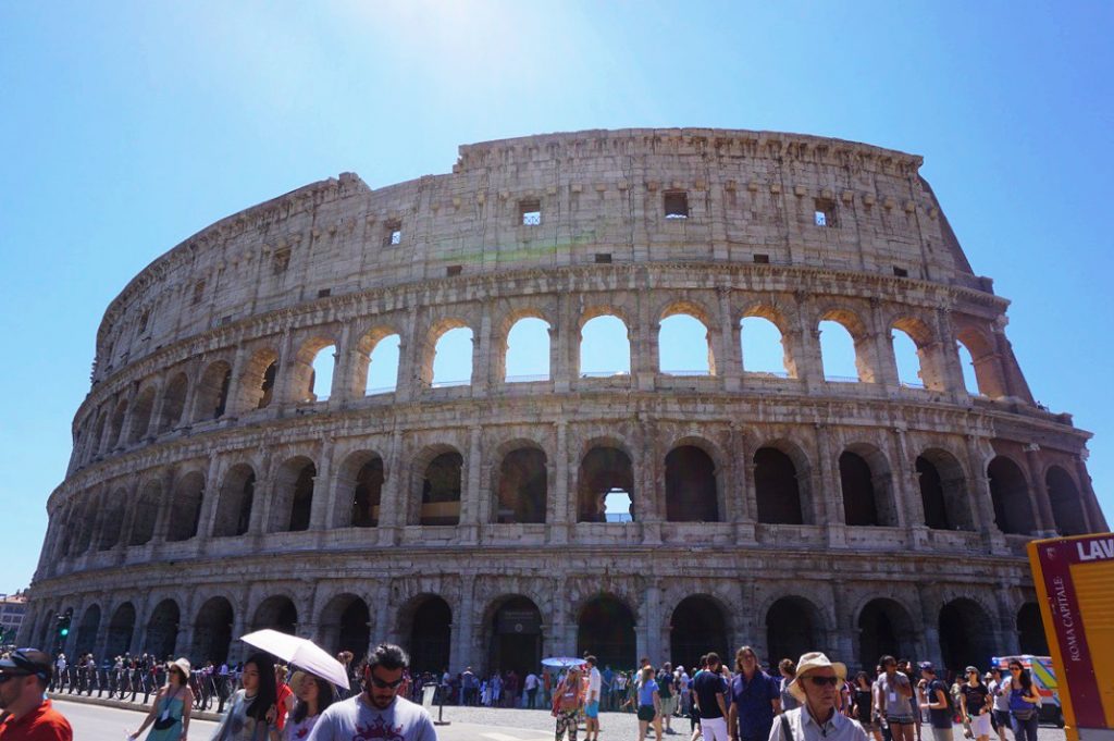 people gathered outside colosseum with sun shining through