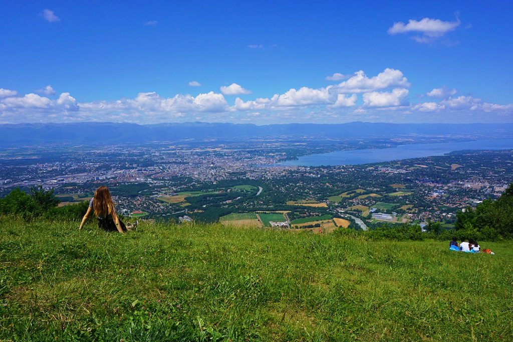 girl sitting in grass looking at geneva from a mountain