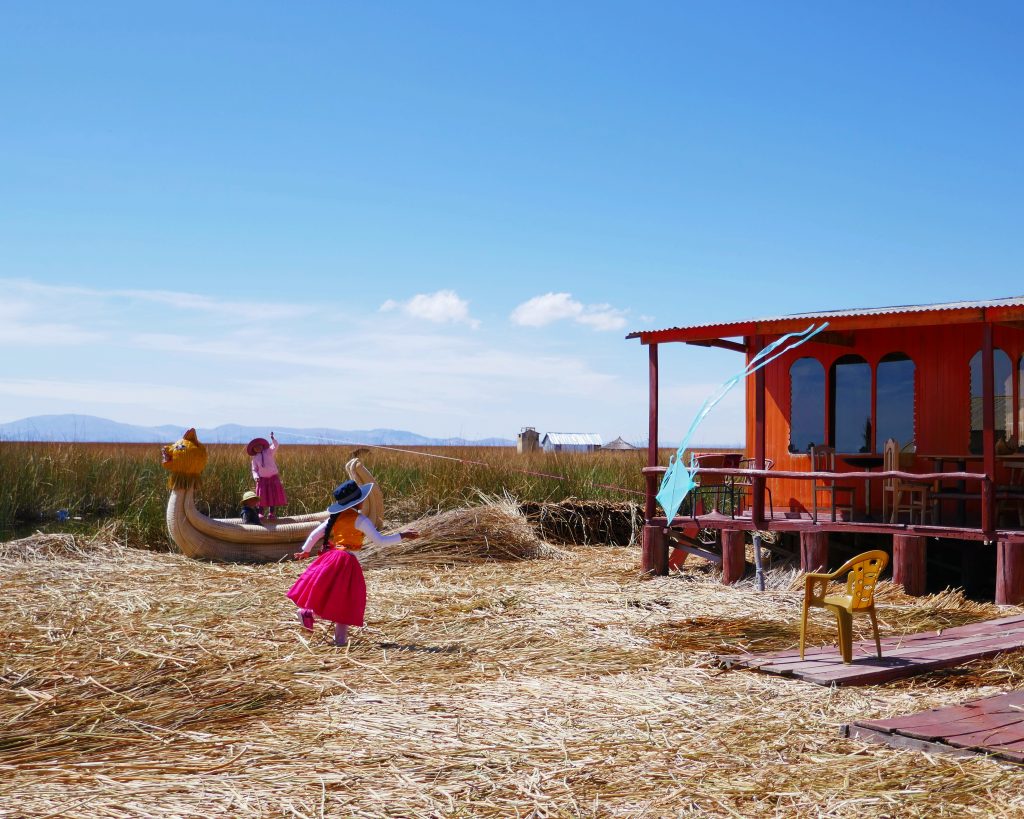 children in traditional uros clothing playing with a kite on a floating island