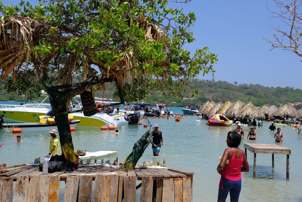 woman standing next to a tree on the rosario islands looking out at the cholon ocean bar on a sunny day in colombia