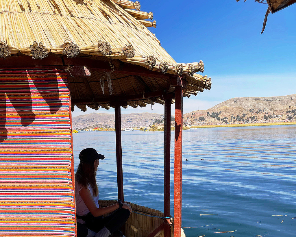 silhouette of girl in traditional hay hut looking at lake titicaca peru