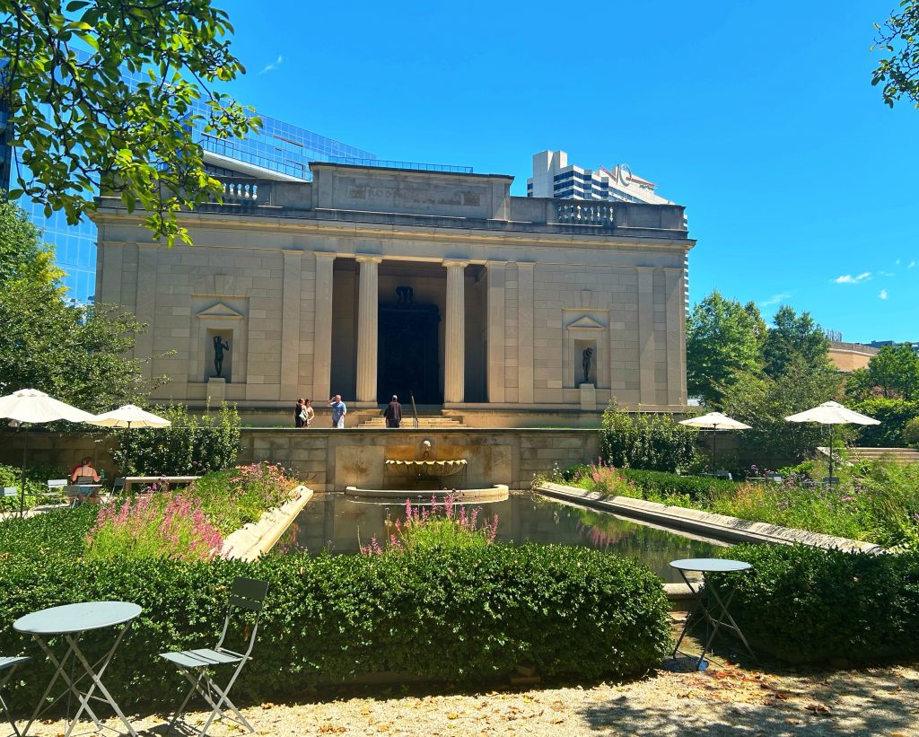 back garden of the rodin museum with rectangular pond, green bushes, and pink flowers