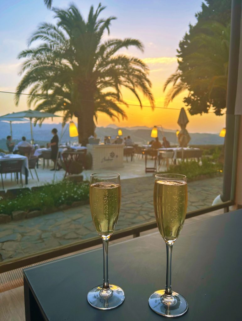 two champagne glasses in front of a restaurant patio with a sunset