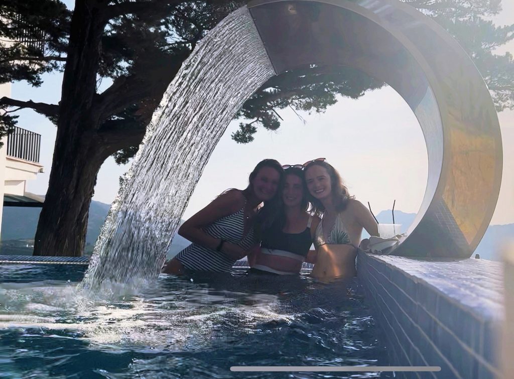 three girls posing under a fountain in the pool