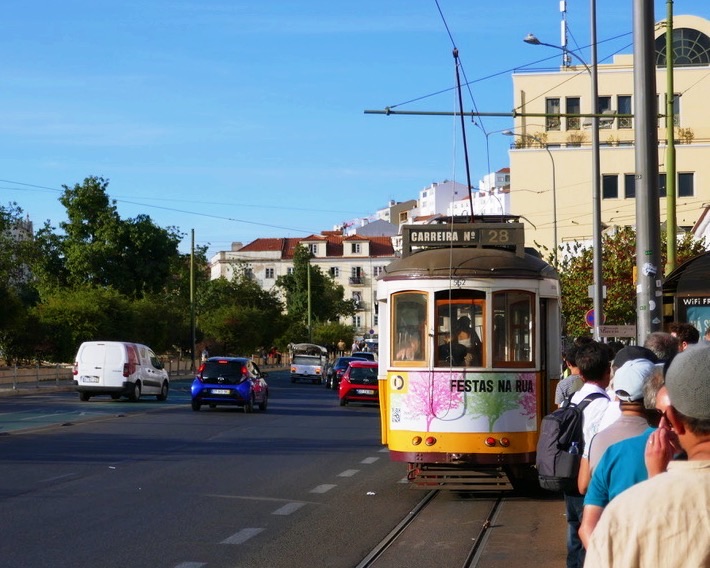 yellow tram 28 trolley in lisbon on a clear day with a queue of people lined up waiting to board