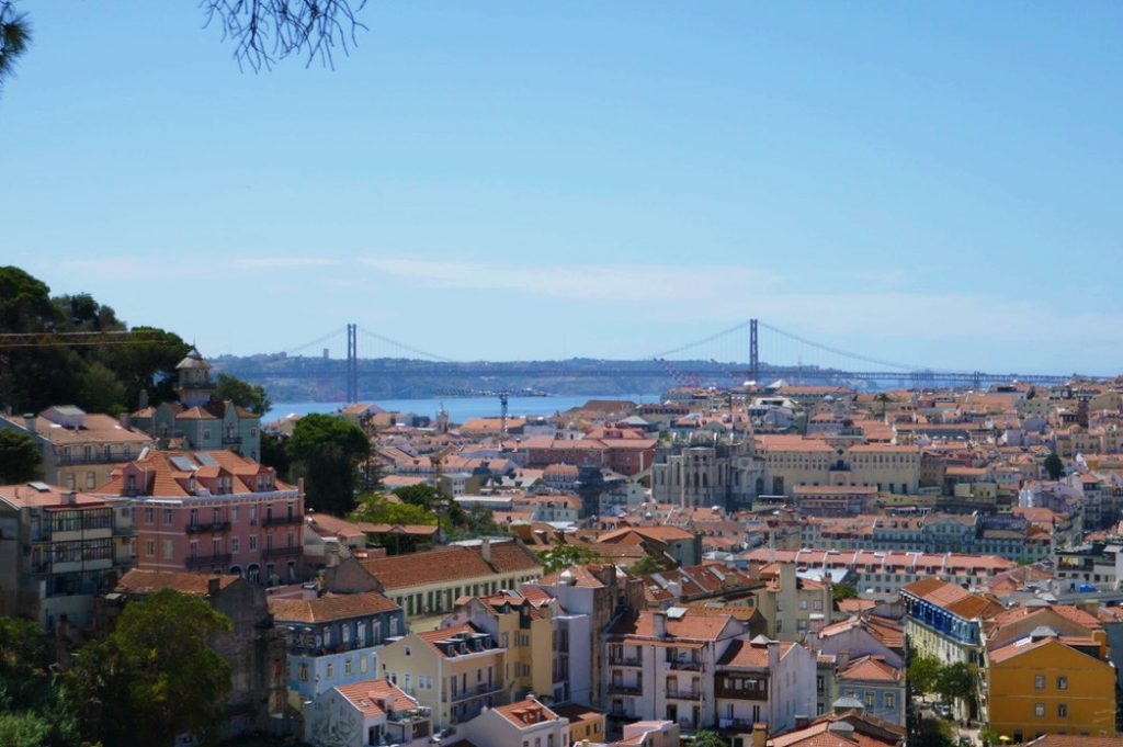 colorful buildings in lisbon with two hanging bridges in the background