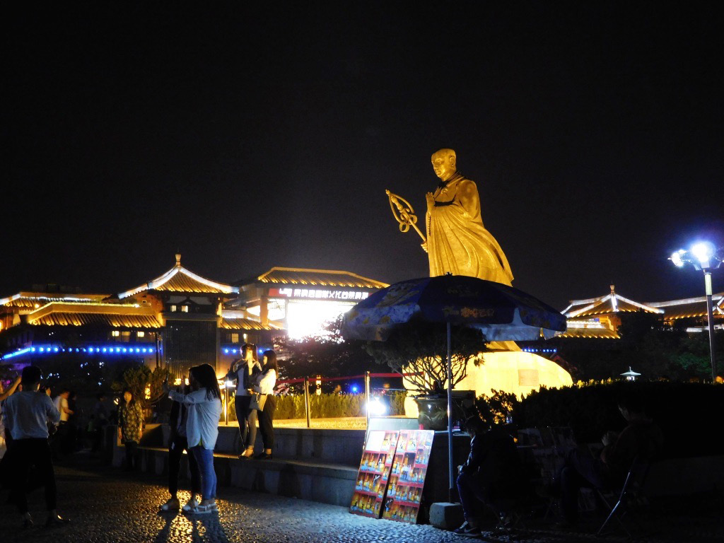 Bronze statue of Master Xuanzang lit by golden lights in the Big Wild Goose Pagoda plaza at night