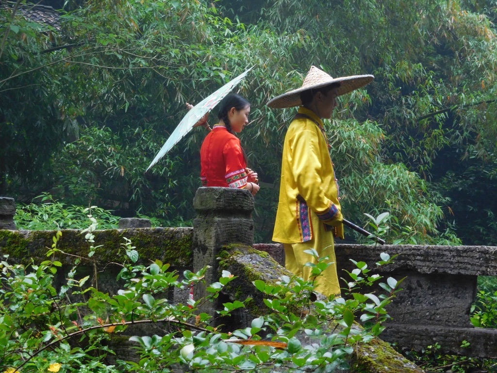 woman with umbrella and man in hat looking out over a bridge