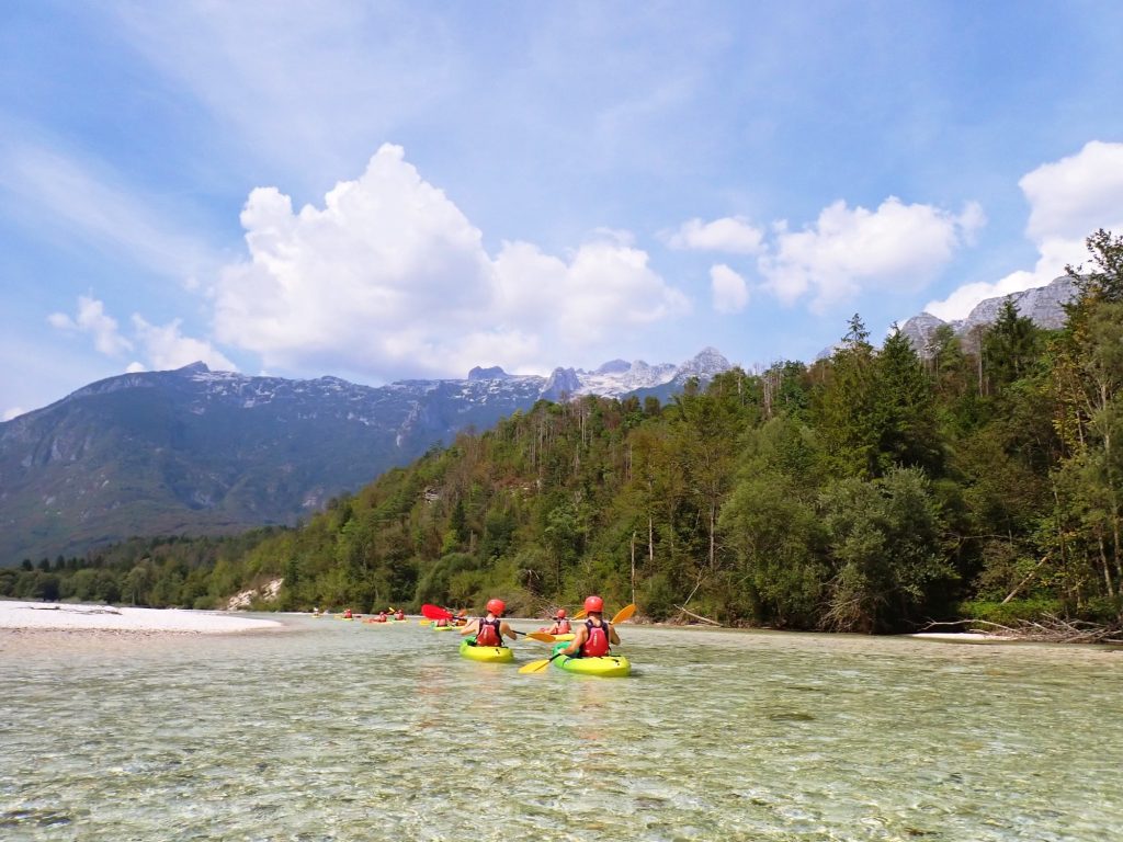 two kayakers on the soca river on a beautiful day with pine trees
