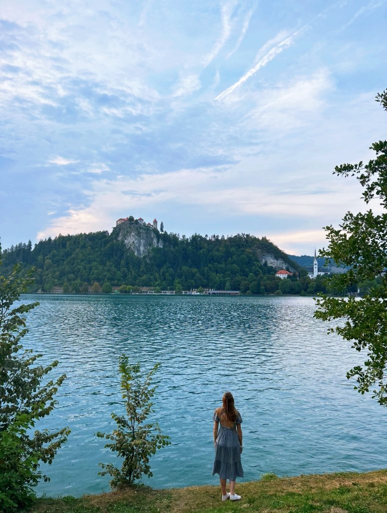 girl in dress standing next to lake bled on a cloudy day