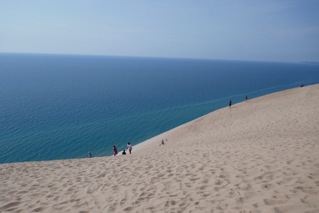 people walking on big sand dunes with ocean in backdrop