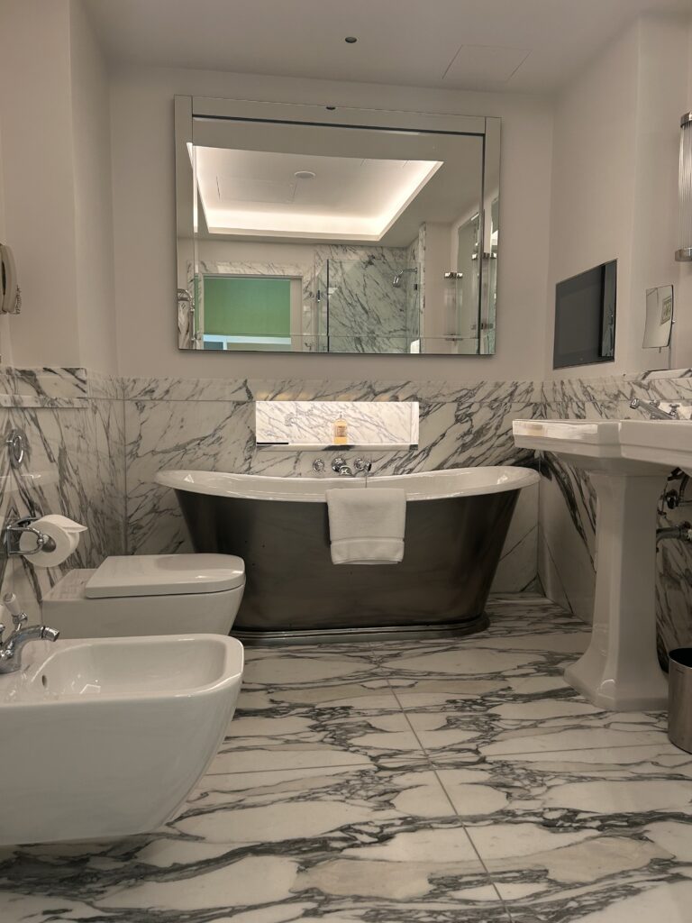 bathtub behind a toiler and bidet with marbled flooring