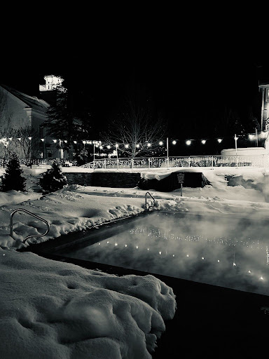 steam rising off of a heated pool surrounded by snow in the dark